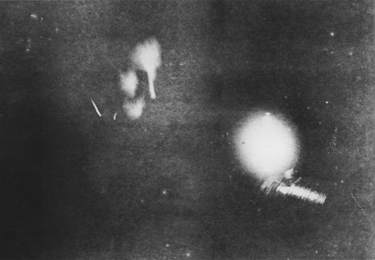 Dark, grainy photograph of a glowing orb and blurred luminous forms