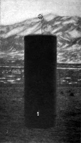 A tall dark cylinder standing on the plain, a small light glowing at its base and snow-covered mountains behind