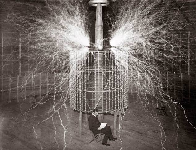 Tesla seated in a chair reading a book beneath the magnifying transmitter as electrical discharges fill the room